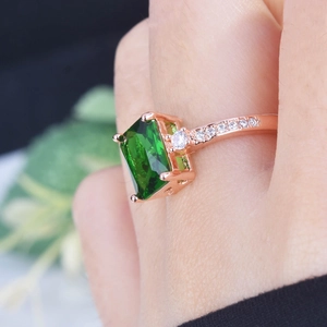 Macro shot of 18K rose gold ring featuring emerald-cut green stone and side diamonds