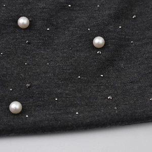 Detail of dark grey knit fabric with white pearls and silver studs on winter beanie