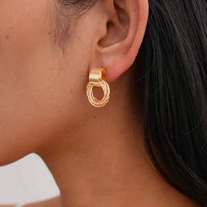 Close-up of golden interlocking textured link earrings shown on a model's ear