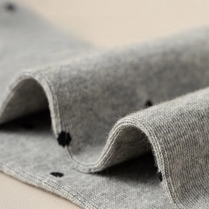 Detail of grey knitted cotton fabric with black polka dots showing soft texture