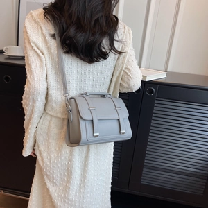 Gray PU leather crossbody bag with top handle shown on a model in an elegant room
