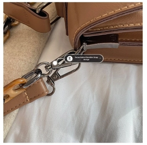 Detail of detachable strap with dark gunmetal clasp and amber resin ring on brown leather bag