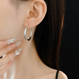 Close-up of polished silver hoop earrings worn by a model against a black background