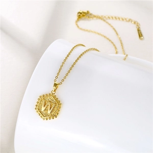 Macro view of gold hexagonal pendant with letter W and beaded edge on fine chain