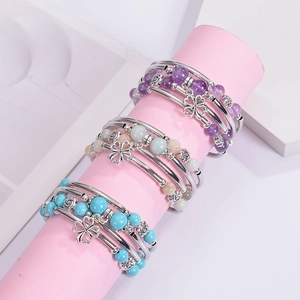 Macro detail of layered beaded bracelets featuring clover and flower metal pendants