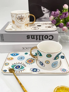 Detail of ceramic Evil Eye coffee cups with gold handles and matching saucers on books