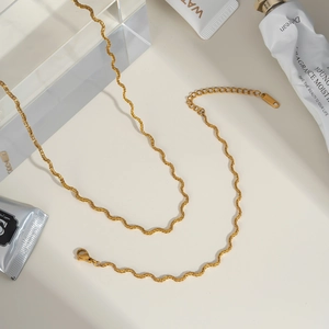 Macro view of gold wave chain necklace featuring a thin curved texture and lobster clasp