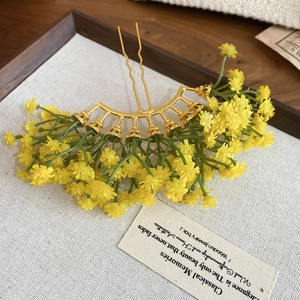 Close-up of golden hair pin with yellow floral fan design on a wooden tray