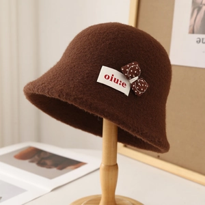 Detailed view of the dark brown wool bucket hat with white polka dot bow and woven label