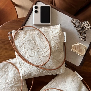 Macro shot of delicate floral leaf embroidery on beige linen crossbody bag fabric