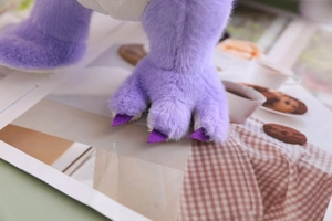Close-up of soft purple plush dinosaur toy feet with stitched claw details and texture