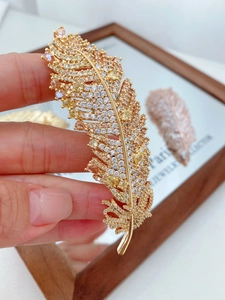 Detail of elegant gold feather brooch with colorful pavé crystals held in hand