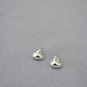 Macro view of mirror polished silver oval stud earrings on gray textured fabric