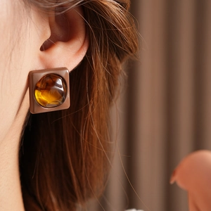 Detail view of brown square earring with amber resin stone on model's ear