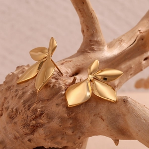 Macro detail of gold-plated stainless steel leaf earrings on a natural wood branch