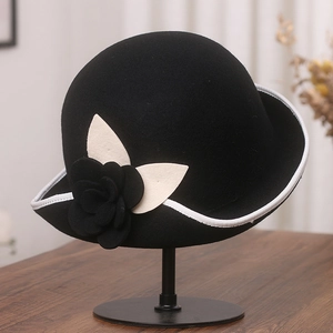 Detail of black wool felt hat with white contrast trim and side floral embellishment