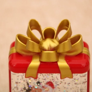 Close-up of red Christmas gift box water globe with a golden bow and sparkling sequins