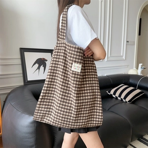 Detail of checkered corduroy tote bag featuring a brand label and wide shoulder strap