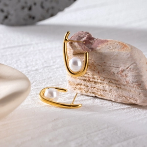 Vue macro de boucles d'oreilles en U dorées avec perles blanches sur un fond de pierre naturelle