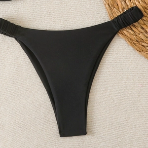 Détail du bas de bikini noir échancré avec bretelles froncées sur fond de vacances d'été