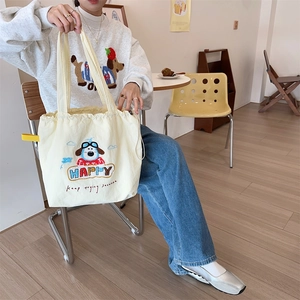 Close-up of cream canvas drawstring tote bag featuring detailed cute puppy embroidery