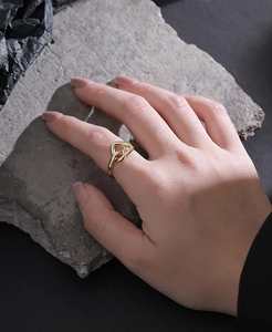Detail shot of a gold interlaced heart ring worn on a finger against a dark rock background
