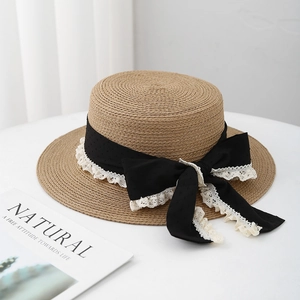 Detail of natural straw boater hat featuring a black ribbon bow and white lace trim