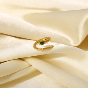 Detail of 18K gold plated snake ring with green zircon eye on beige silk fabric