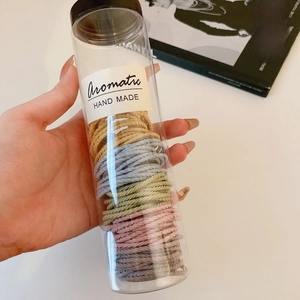 Hand holding a cylinder jar of colorful handmade elastic hair bands on a white desk