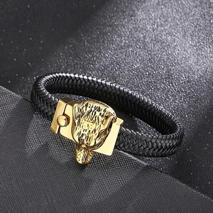 Detail of men's woven leather bracelet with golden wolf head clasp and metal relief