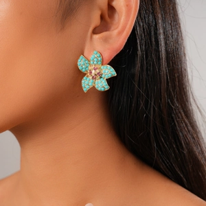 Close-up of vintage floral earrings with turquoise petals and pink gemstones on ear