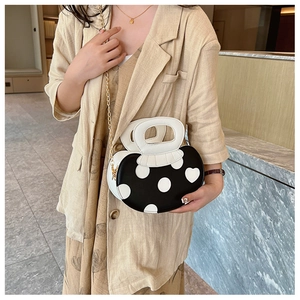Detail of black and white polka dot handbag with mushroom handles and gold chain strap