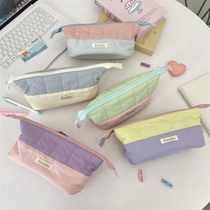 Quilted pastel pencil cases in various colors on a desktop with stationery and laptop