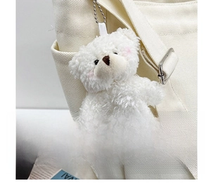 Close-up of a white teddy bear plush keychain accessory on a canvas shoulder bag