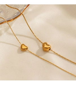 Détail de deux pendentifs cœur dorés sur une fine chaîne box sur du tissu en soie