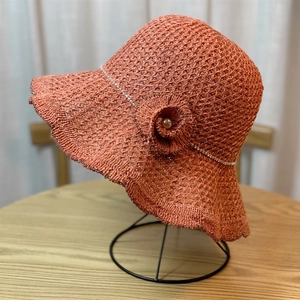 Detail of orange knitted sun hat featuring wavy brim, sparkling rhinestones and pearl flower
