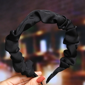 Close-up of black pleated headband with satin finish held by hand for detail