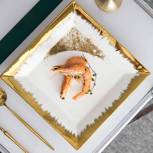 Minimalist white ceramic square plate with gold rim featuring cooked shrimp and herbs