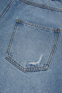 Vue détaillée de la texture du denim, des coutures et des trous usés sur la poche jean