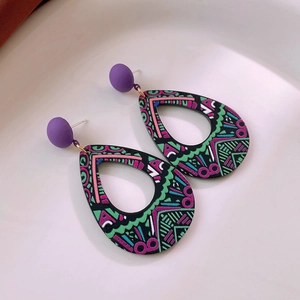 Close-up of teardrop earrings with geometric patterns on a white ceramic tray