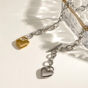 Two-tone 18k gold and silver heart padlock necklace with toggle clasp on cream backdrop