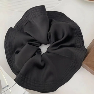 Macro shot of large black satin scrunchie showing glossy fabric texture and pleats