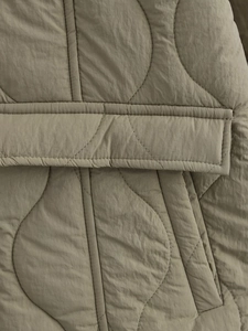 Close-up of army green quilted cotton jacket showing detailed curved stitching texture