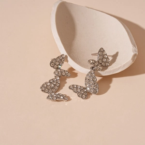 Detail shot of silver butterfly drop earrings with shimmering crystals on ceramic plate