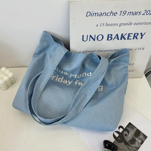 Dettaglio della borsa tote in denim azzurro con ricami bianchi e accessori eleganti