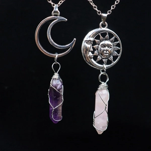 Detail of silver moon pendants with wrapped amethyst and rose quartz stones on black background