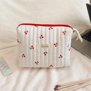 Detail of a white cotton quilted cherry print makeup bag with red zipper and branding