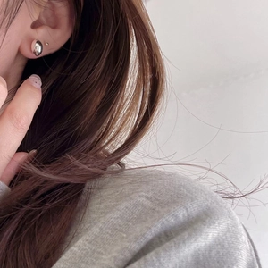 Close-up of minimalist sterling silver bean studs on model's ear with soft lighting