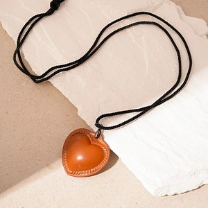 Detail of a brown leather heart pendant with hand-stitched edges and a black braided cord