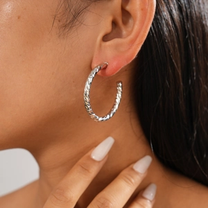 Close-up of a model wearing large silver C-shaped hoop earrings with diamond-cut texture